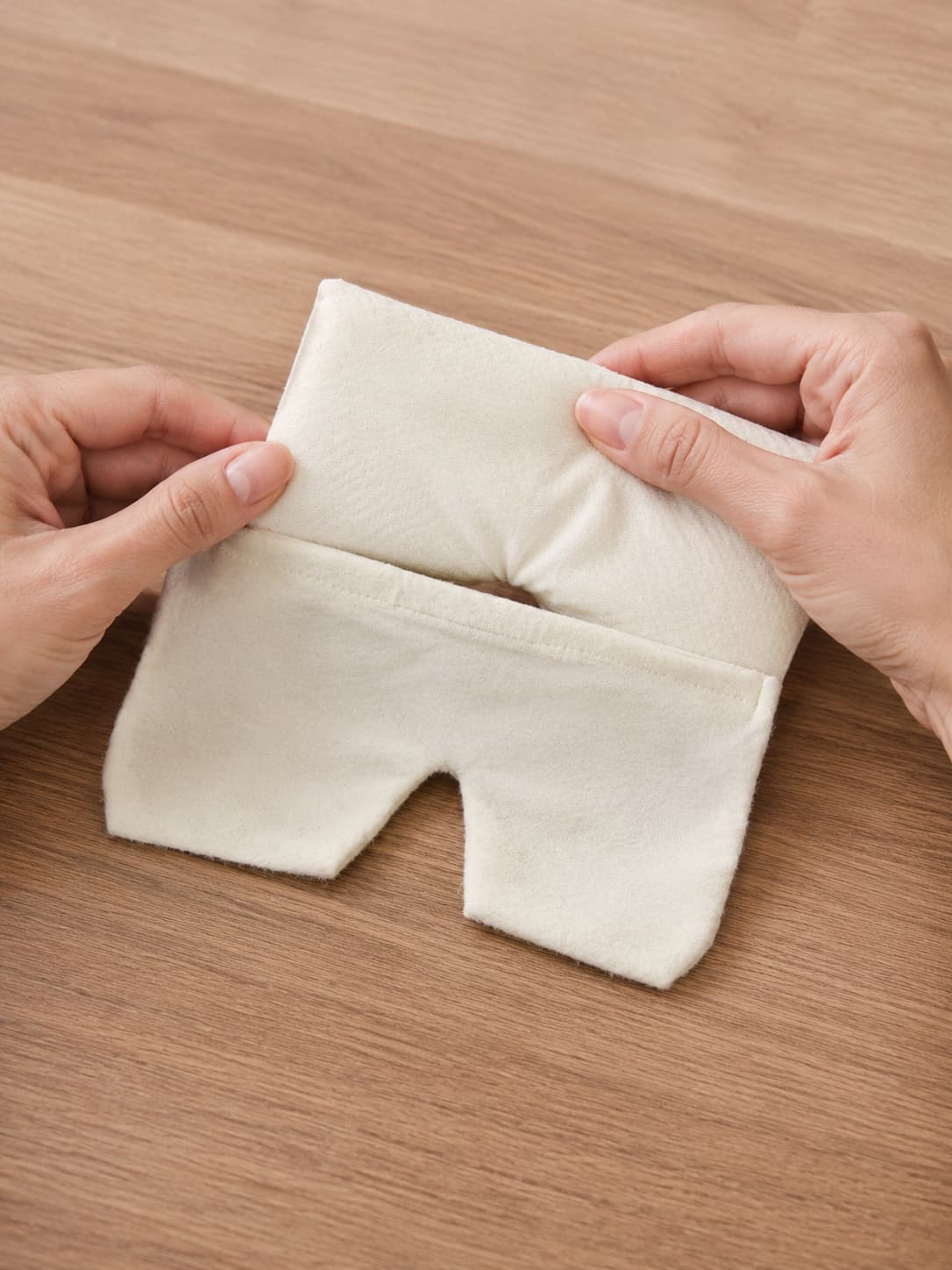 Mains tenant une housse repose-yeux en flanelle blanche, montrant la forme et l'ouverture du produit
